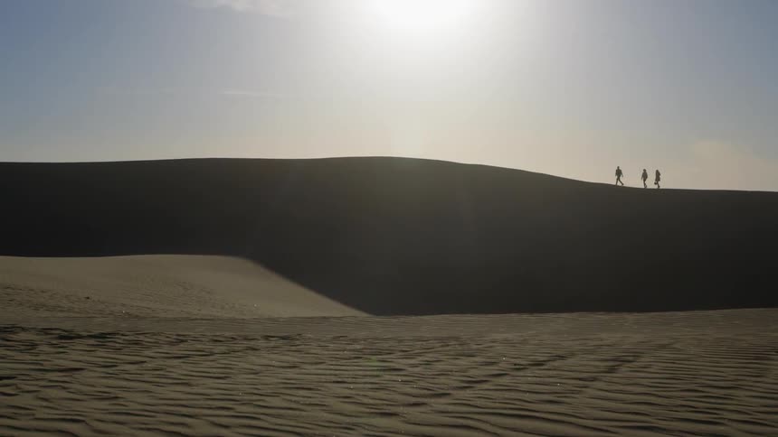 Three people walking on the sand under a blue sky