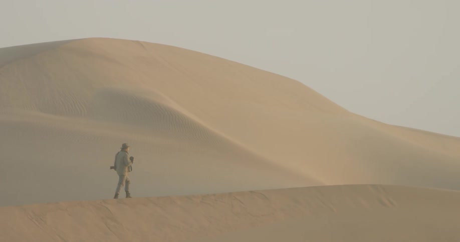 A photographer walks in a sandy desert