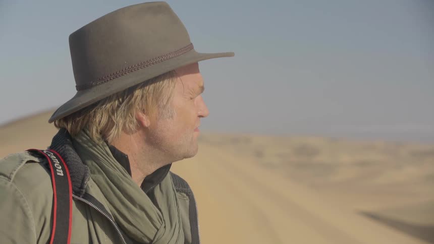 A photographer stands in a desert on a sunny day