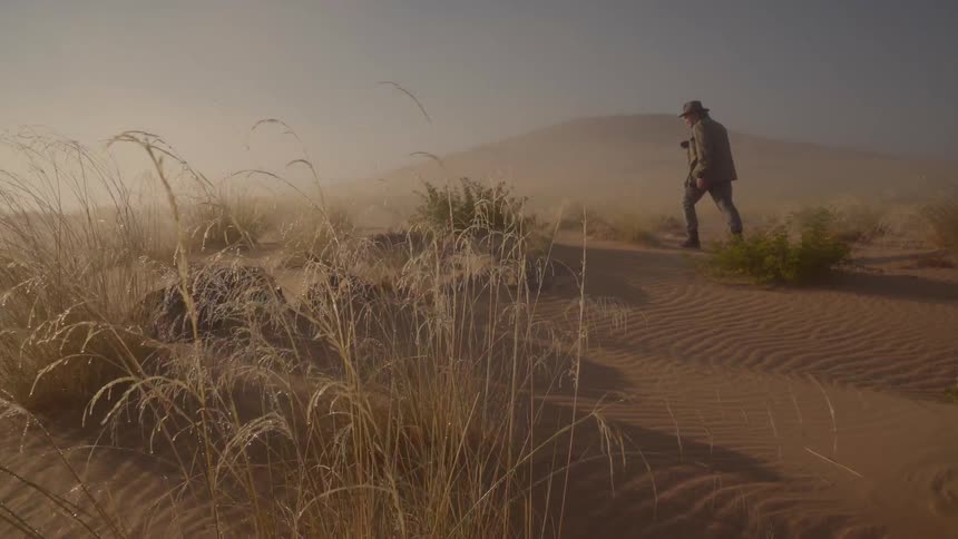 A man carries a camera as he hikes in the desert