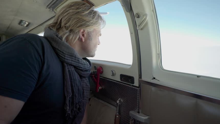 A man looks out the window while riding in a small airplane