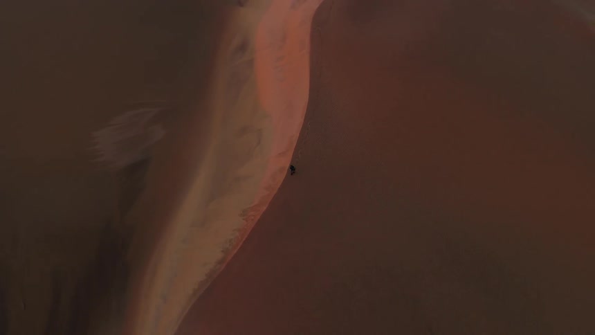 Aerial view of person walking on sand dunes at sunset