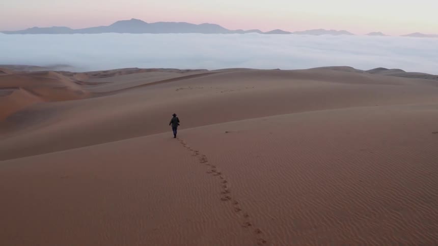 A person is walking in the desert towards the water