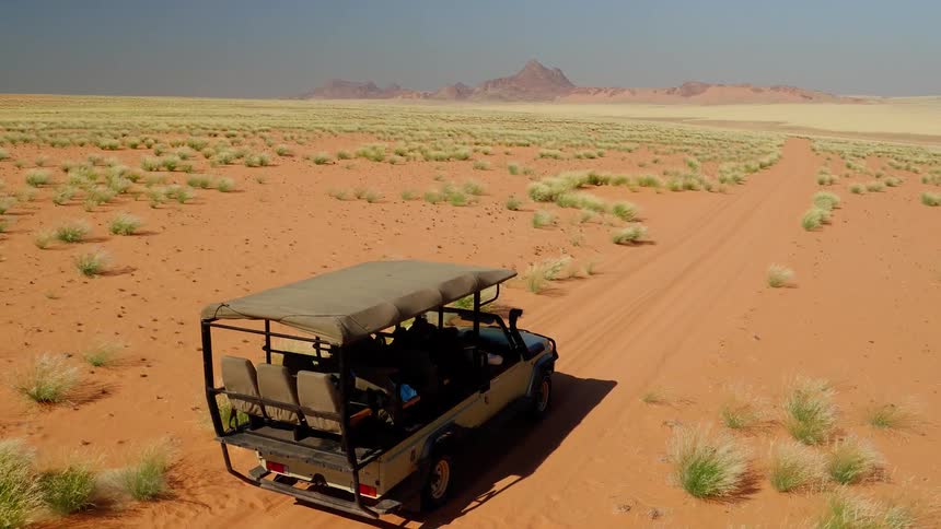 The desert is very windy as a man walks towards his vehicle
