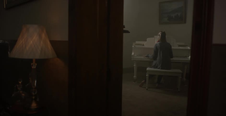 A woman is walking towards a piano in a house