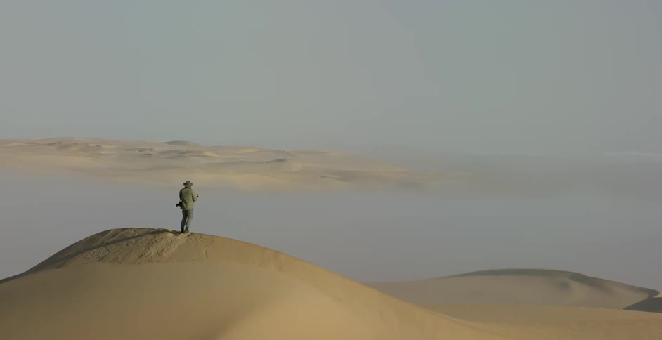 A photographer stands on a sand dune in a desert