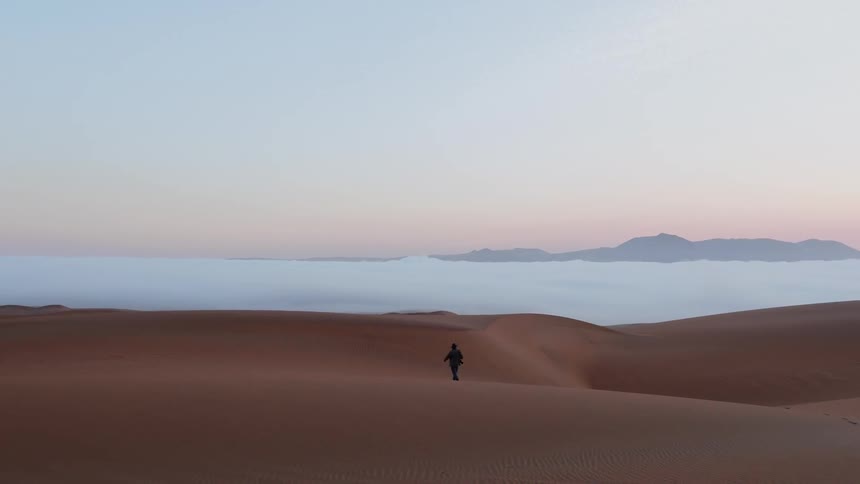 A man is walking along the sand in the desert
