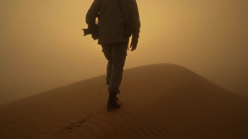 A man is walking up a sand dune in the desert