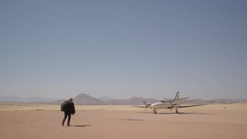 A man walks toward a small airplane on a dirt runway