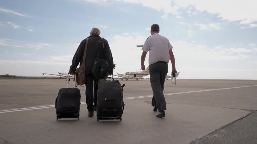 A man follows dragging luggage behind towards an airplane