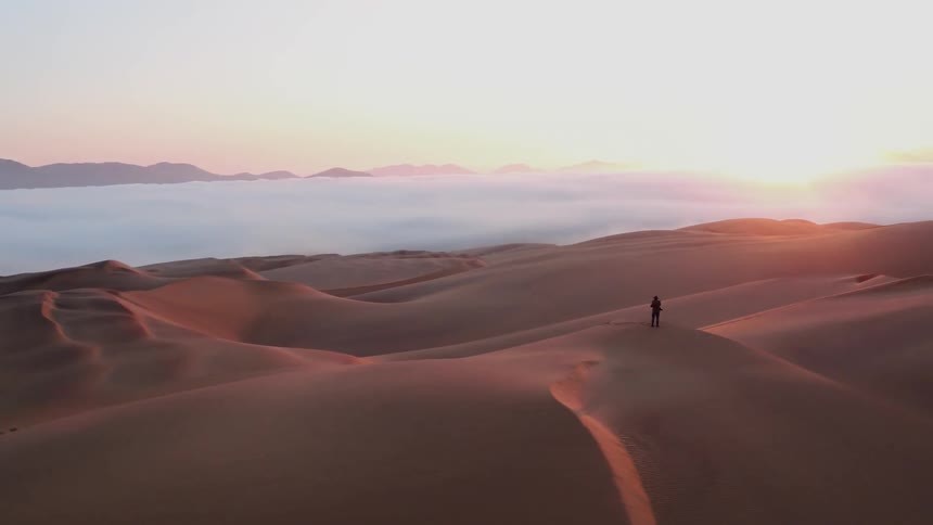 A hiker stands on a sand dune in the desert at sunset