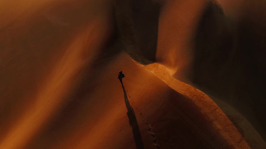 A man is walking in the desert being filmed by a drone