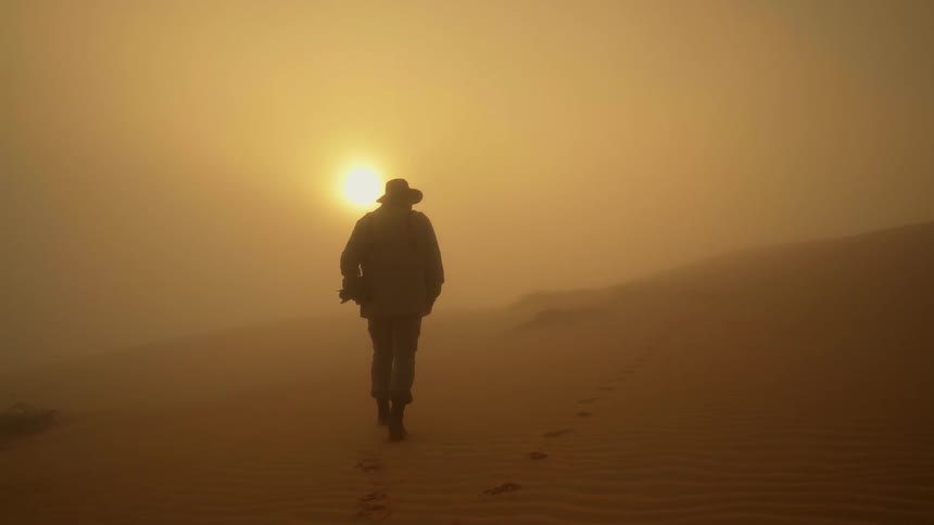 A man is walking towards the sun in the desert