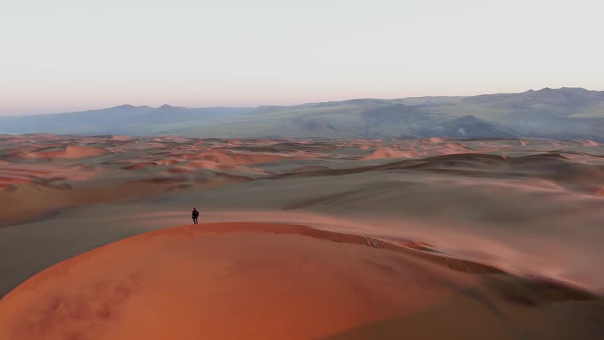 A hiker walks on a sand dune in a desert at sunset