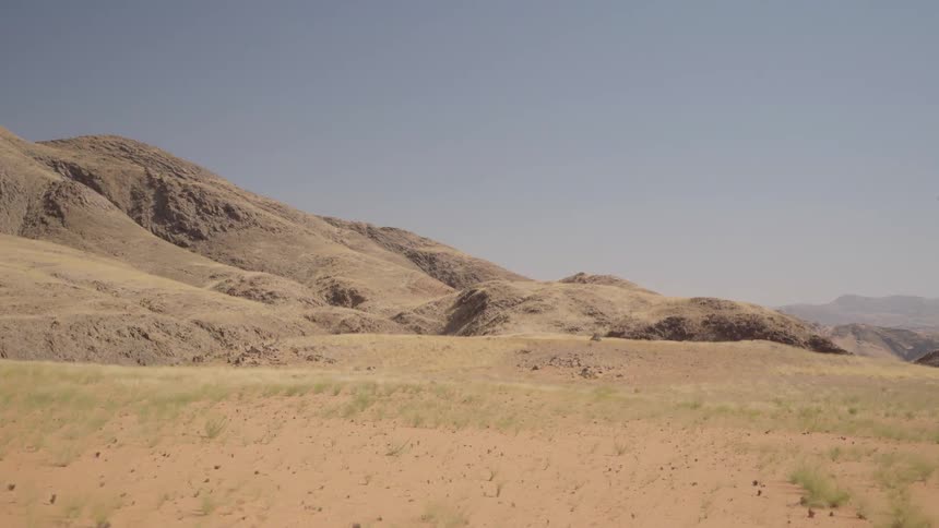 Grass and hills are being filmed from a moving vehicle