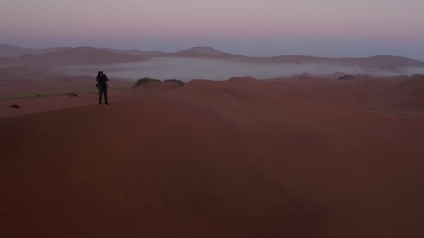 A man is standing on a sand dune taking photographs
