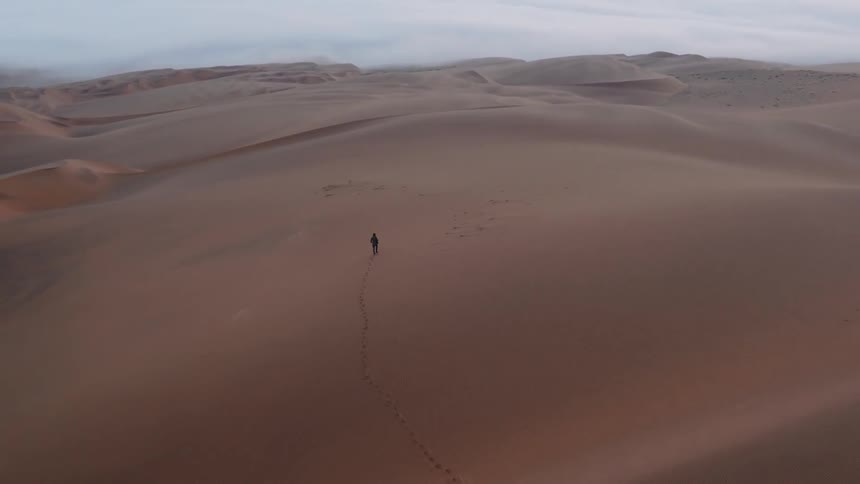 A man being filmed by a drone is walking alone in the desert