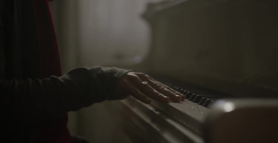 A woman is sitting at a piano gently touching the keys