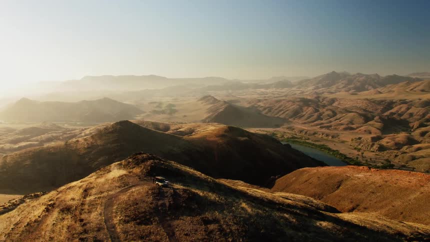 Someone is standing on top of a large hill being filmed from a drone