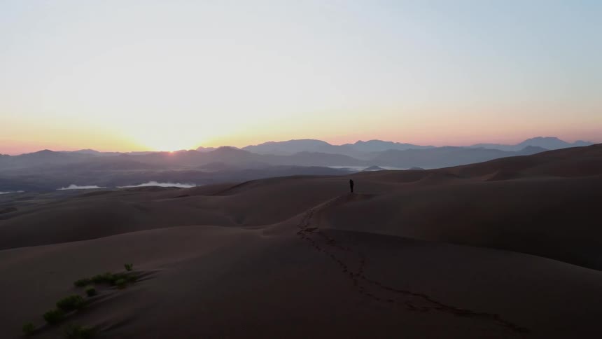 A hiker stands on a sand dune in the desert at sunset