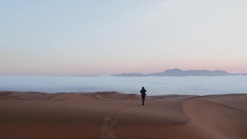 A photographer walks in a desert at sunset