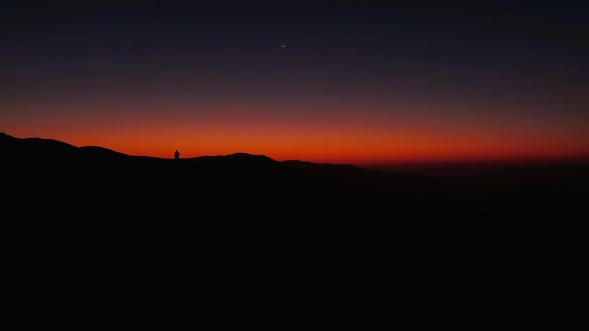 A man is standing on the edge of a mountain at dusk