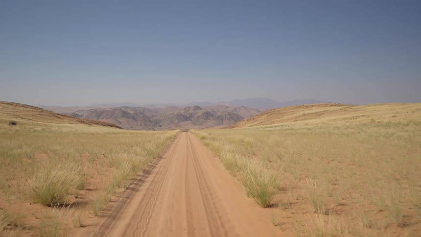 The dirt road has hills on both sides