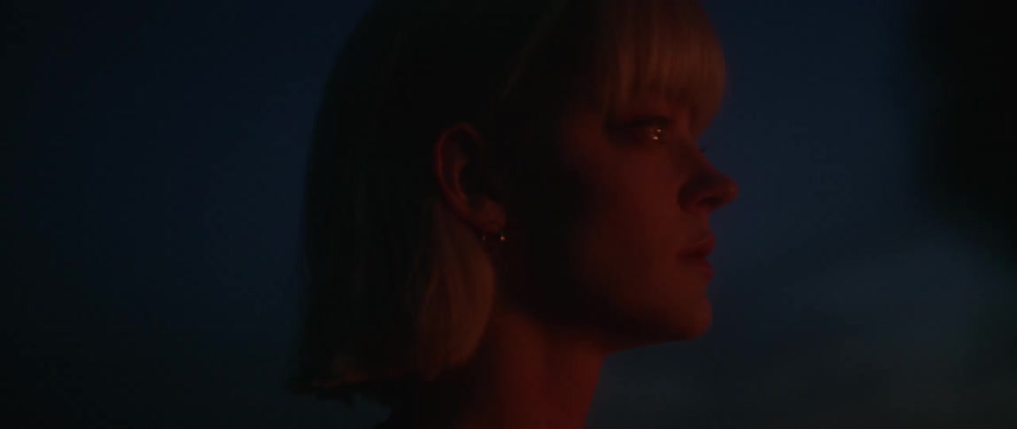 A woman watches as a car burns off screen