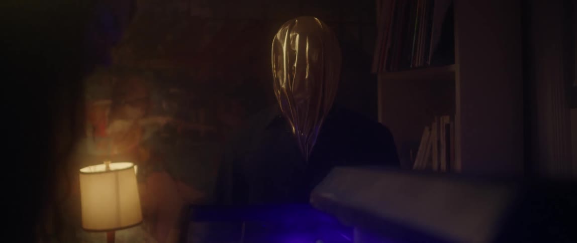 A person with a bag over their head watches a man next to a fish tank