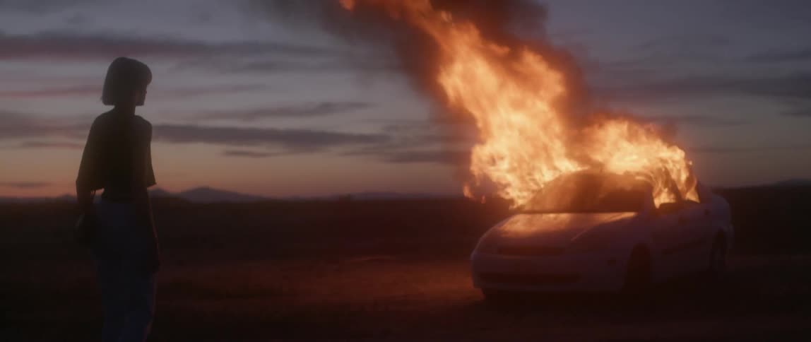 Woman watches a vehicle burn outside at night