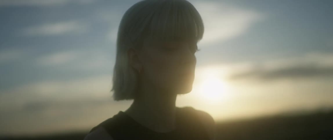 A woman walks outside as the sun sets behind her
