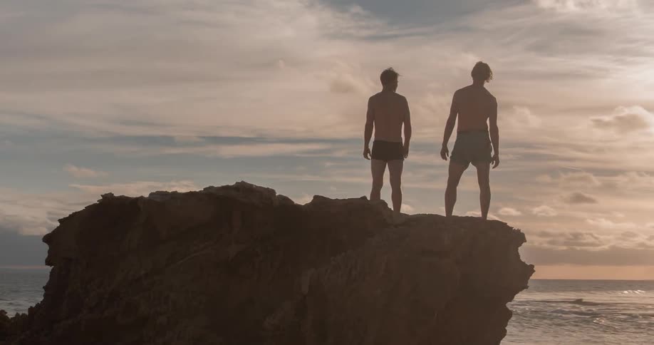 Two men stand on a cliff by the ocean