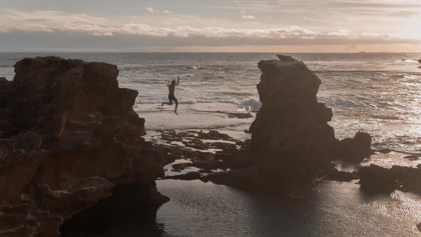 Man jumps off the edge of a cliff into a pool of water