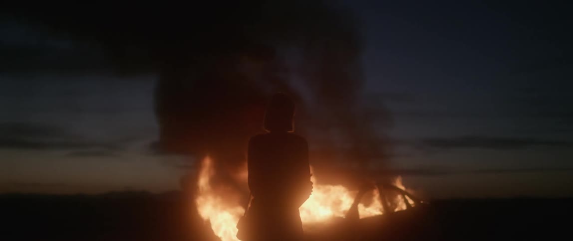A woman watches a car burn