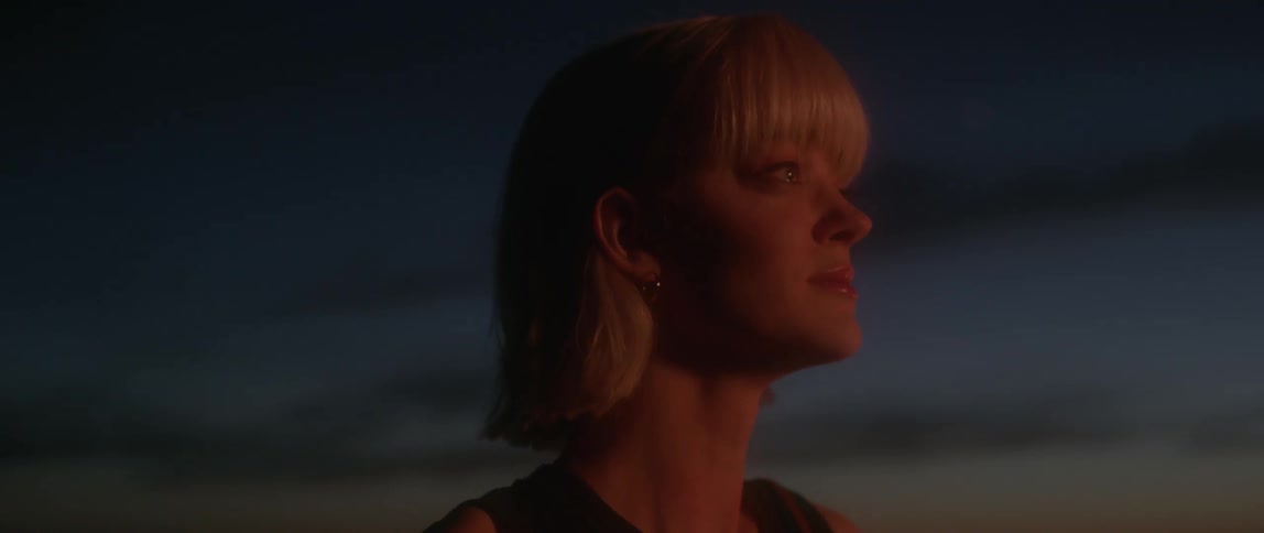 Woman with short blond hair and sleeveless top is under a night sky