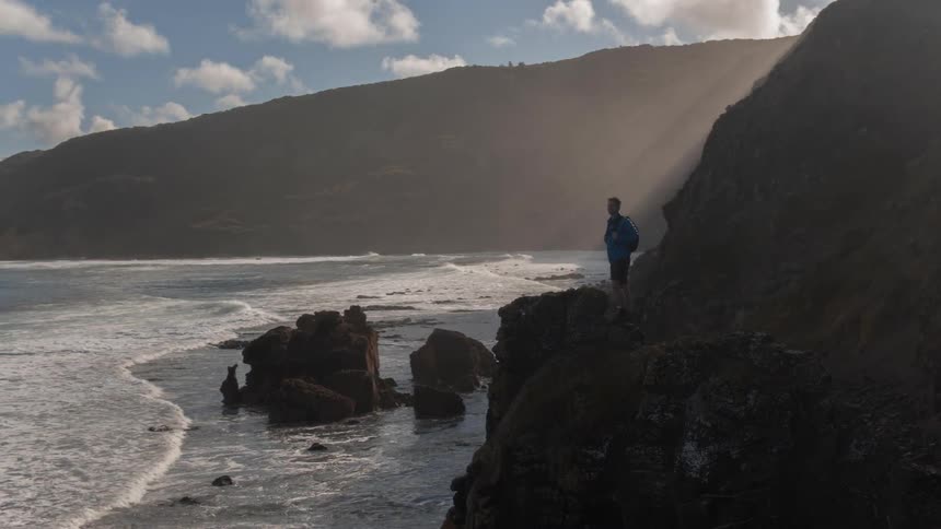Man stands on a small cliff looking out at the water