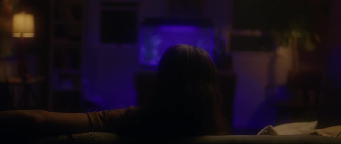 A man is sitting on a couch watching a purple fish tank