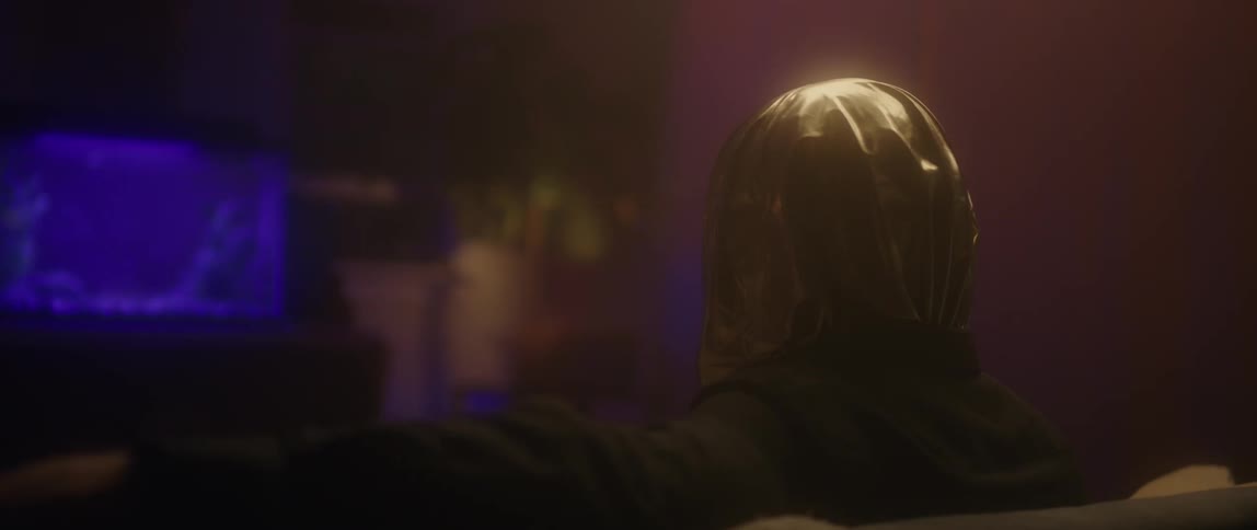 A man is sitting on a couch wearing a gold hood