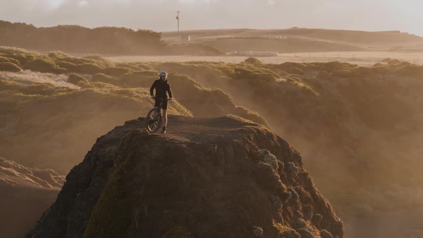A person with a bike is standing on top of a hill overlooking the ocean