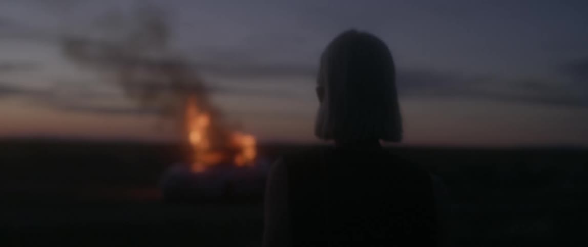 Woman watches a vehicle burn outside at night