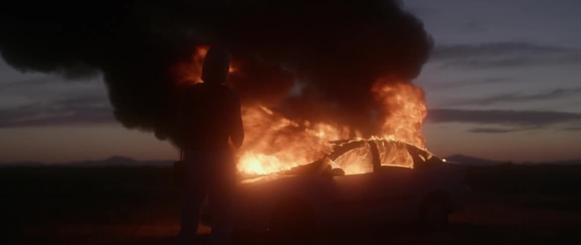 A car fire is out of control as a woman watches