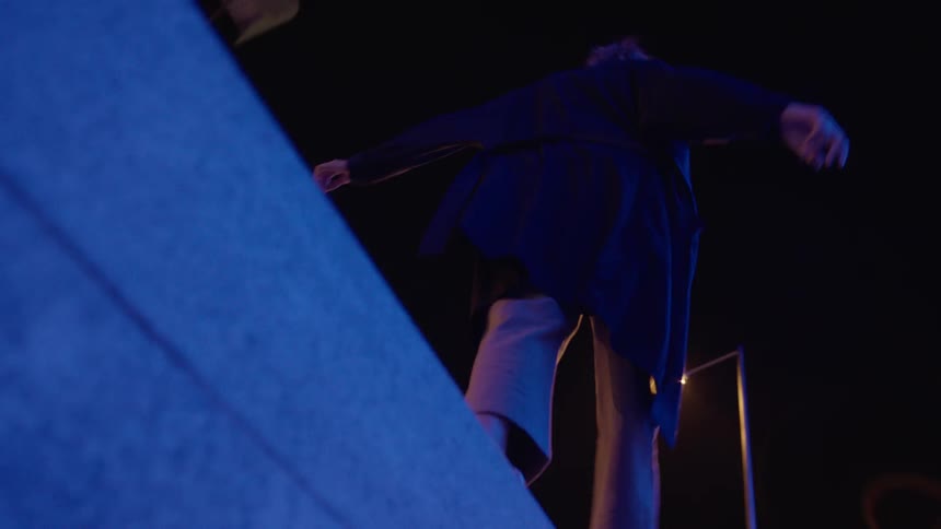 Woman walking and balancing on top of building in city at night