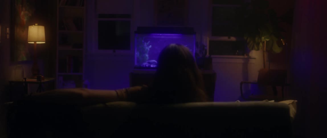 A man with long hair is watching a purple glowing fish tank
