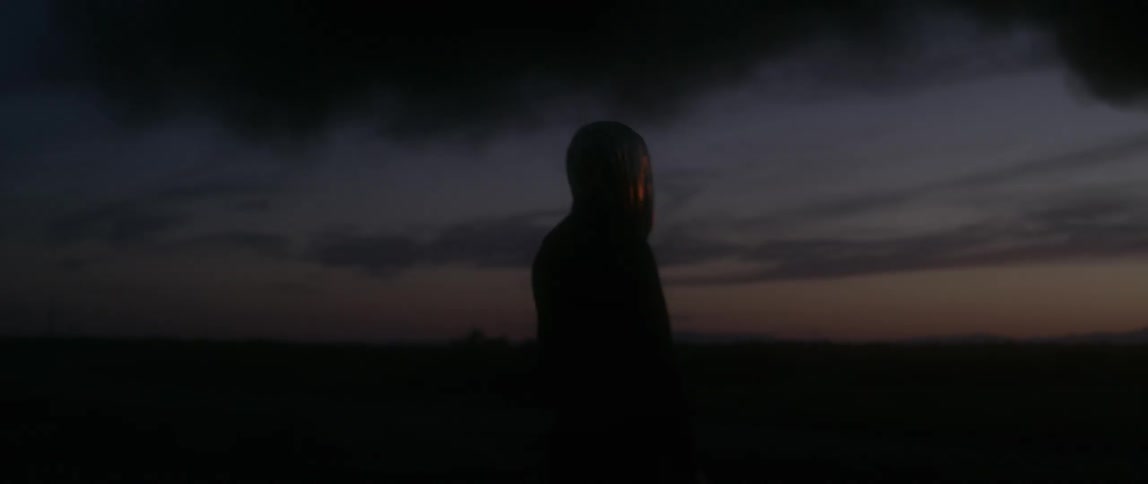 A man wears a hood while standing outside at dusk