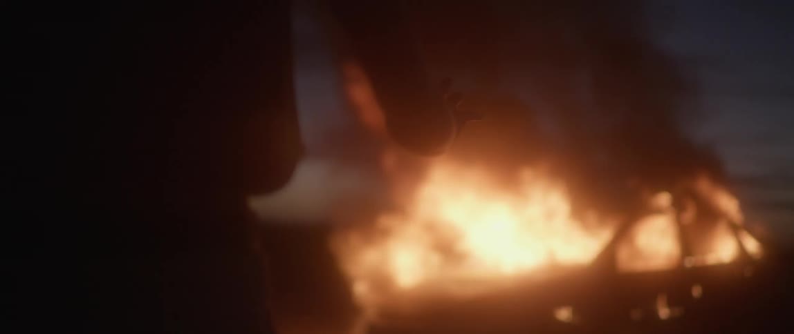 A person looks at a fire and clenches her fists