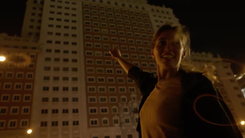 A woman smiles and points at a tall city building