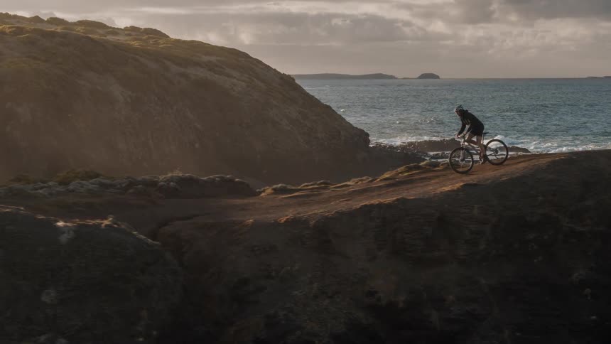 Person riding a bike next to the ocean on top of hills