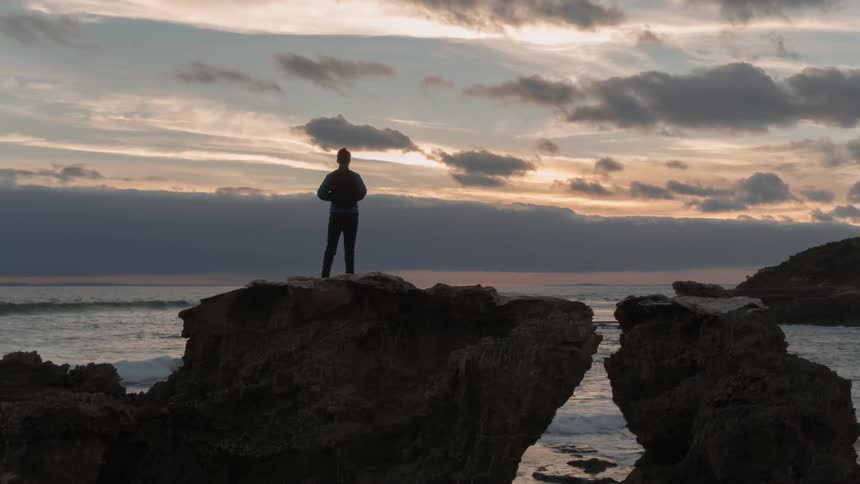 Someone is standing on top of a large rock in front of the ocean