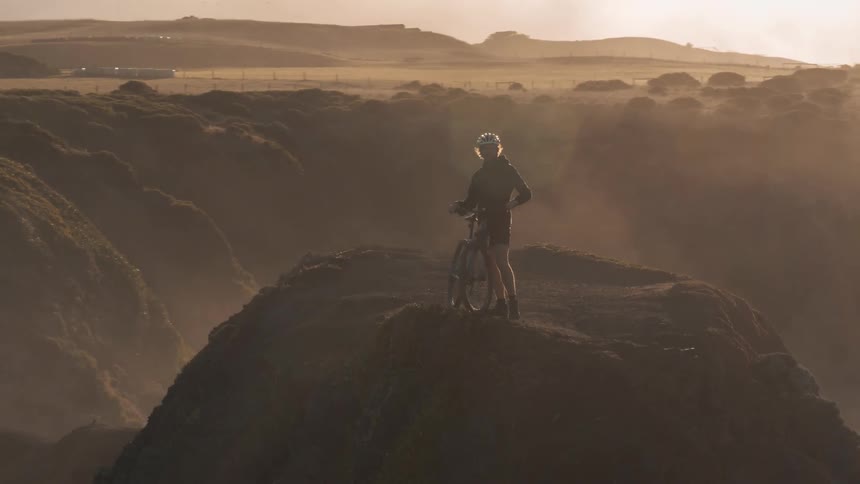 A guy on a bike is standing on top of a large hill