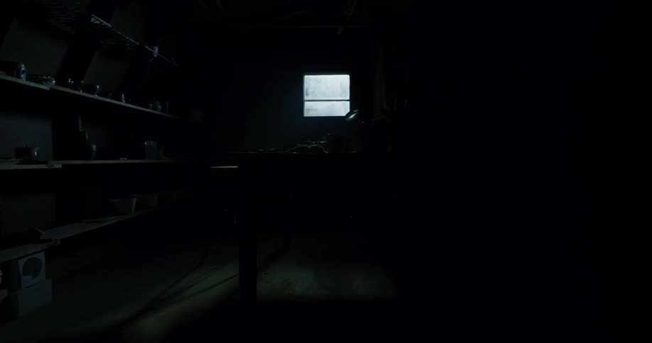 A window in this dark room shows rain outside